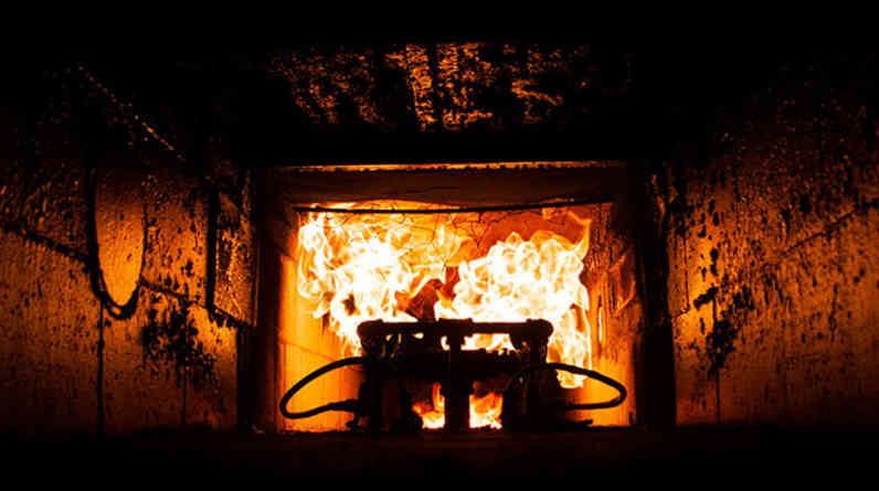 Inside a dark furnace, looking towards the main heating element with fire coming out of it.