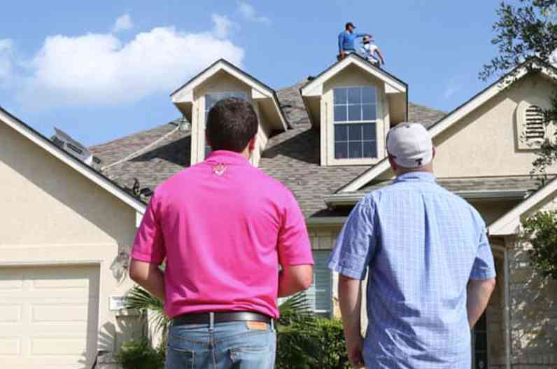 Two males looking up at a residential rooftop.