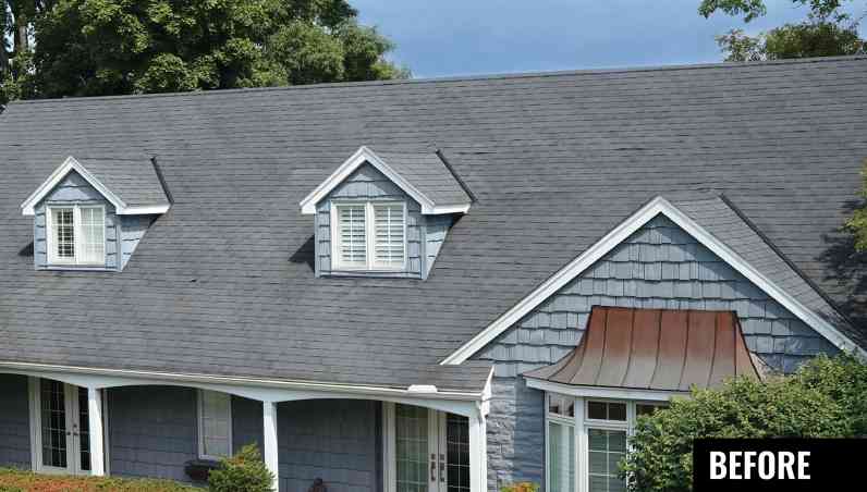 Grey blue house with shake siding, copper awning, white trim, two dormer windows and old grey roof with signs of aging and bald spots.