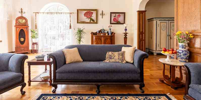 Dark blue traditional furniture shown in a livingroom with three throw pillows, side tables, pictures on the wall and an area rug.