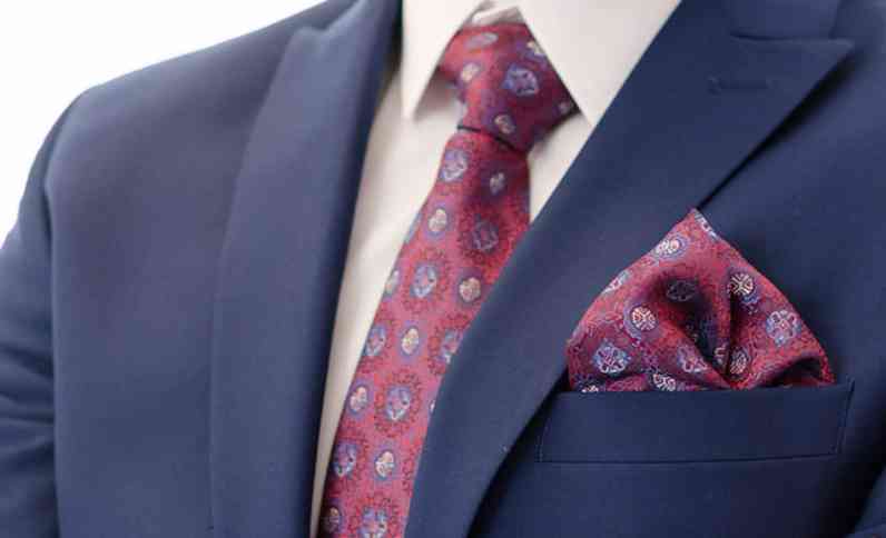 Top portion of a blue suit jacket with burgundy patterned tie