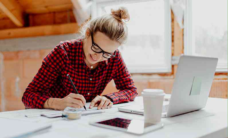 Person sitting at a desk with laptop open, sketching on a piece of paper