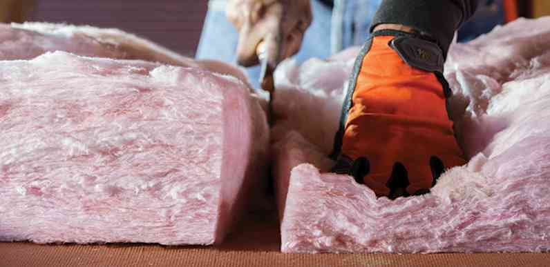 Worker wearing orange work gloves cuts pink insulation