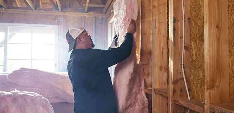 Un installateur tient une nappe d'isolant rose dans une cavité murale.