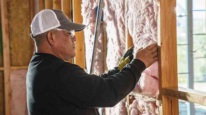 A builder inspects the installation of fiberglass within the wall cavities of a house under construction