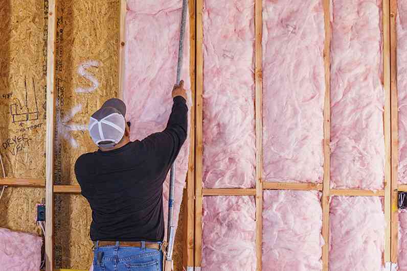 A contractor places pink insulation inside wall cavities.