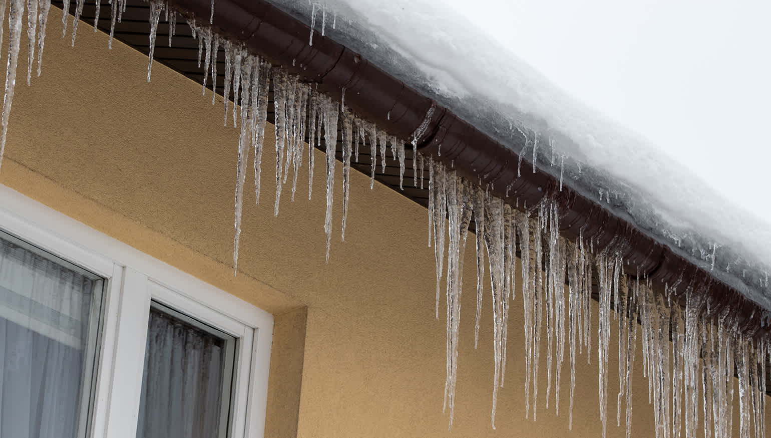 Excessive ice damming on yellow stucco home, and snow built up on the roof.