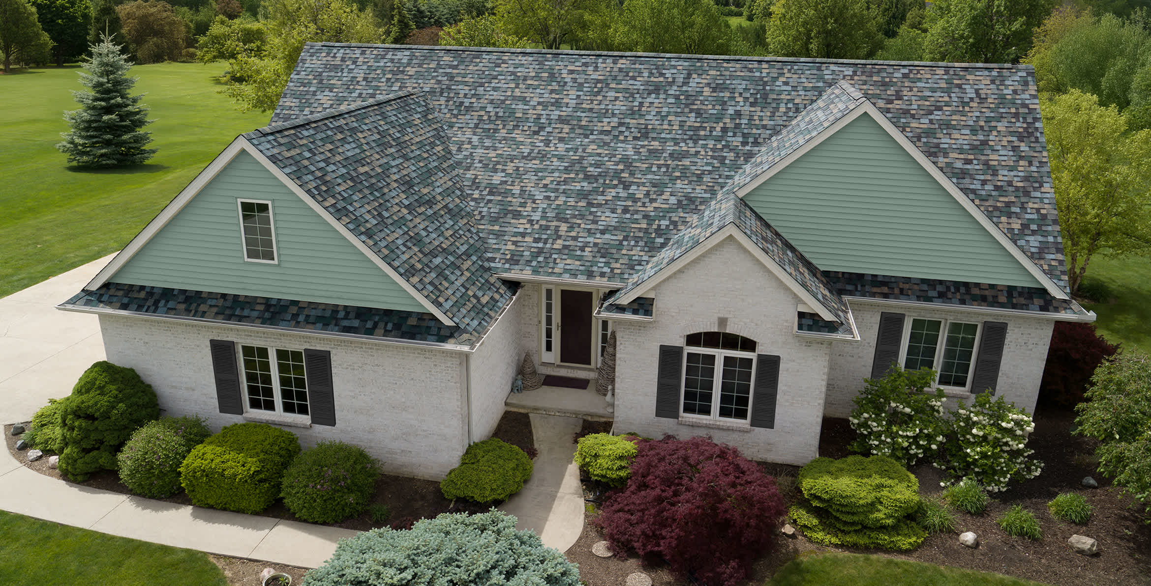 A white brick house sits on a beautifully landscaped yard with new Evergreen Mist roof
