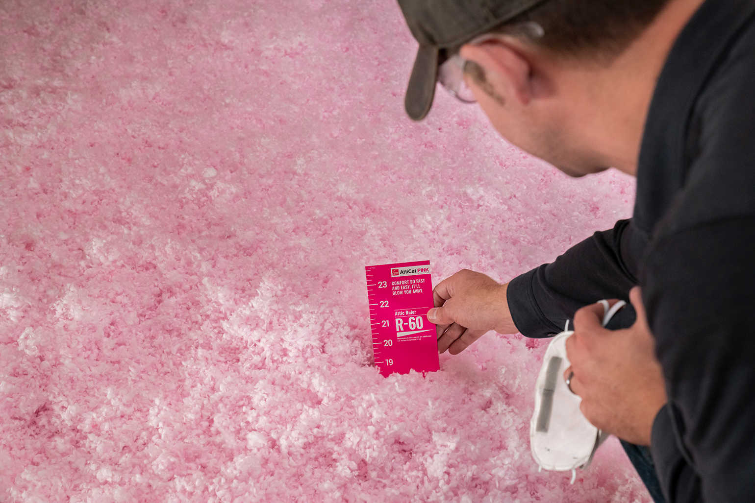 Man measuring AttiCat® PINK loose fill insulation to ensure proper R-Value is achieved