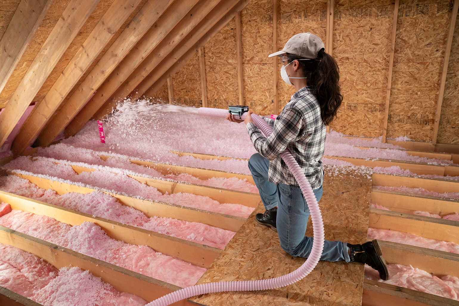 Woman installing AttiCat® blown-in, loose fill insulation covering joists