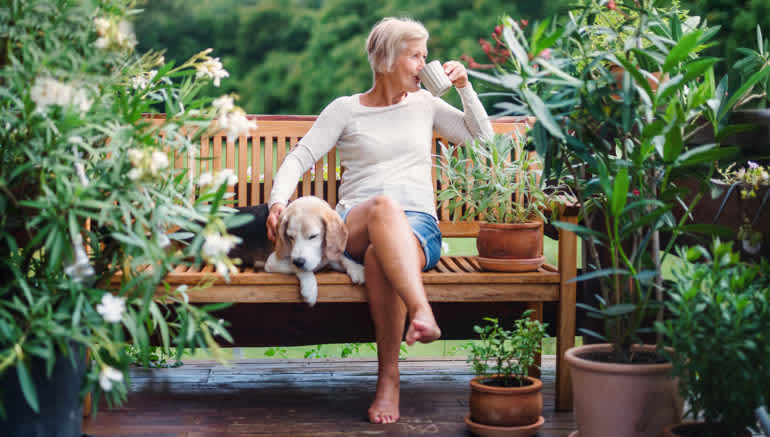 Woman sitting on a bench outdoors, sipping from a coffee mug and sitting next to a dog