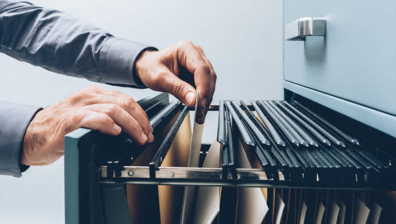 Person's hands looking through folders in a filing cabinet