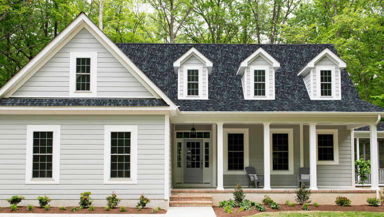 Exterior of a new Cape Cod styled suburban house with recently planted shrubs and grass