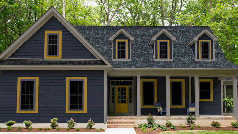 Exterior of a new Cape Cod styled suburban house with blue siding and yellow trim, recently planted shrubs and grass