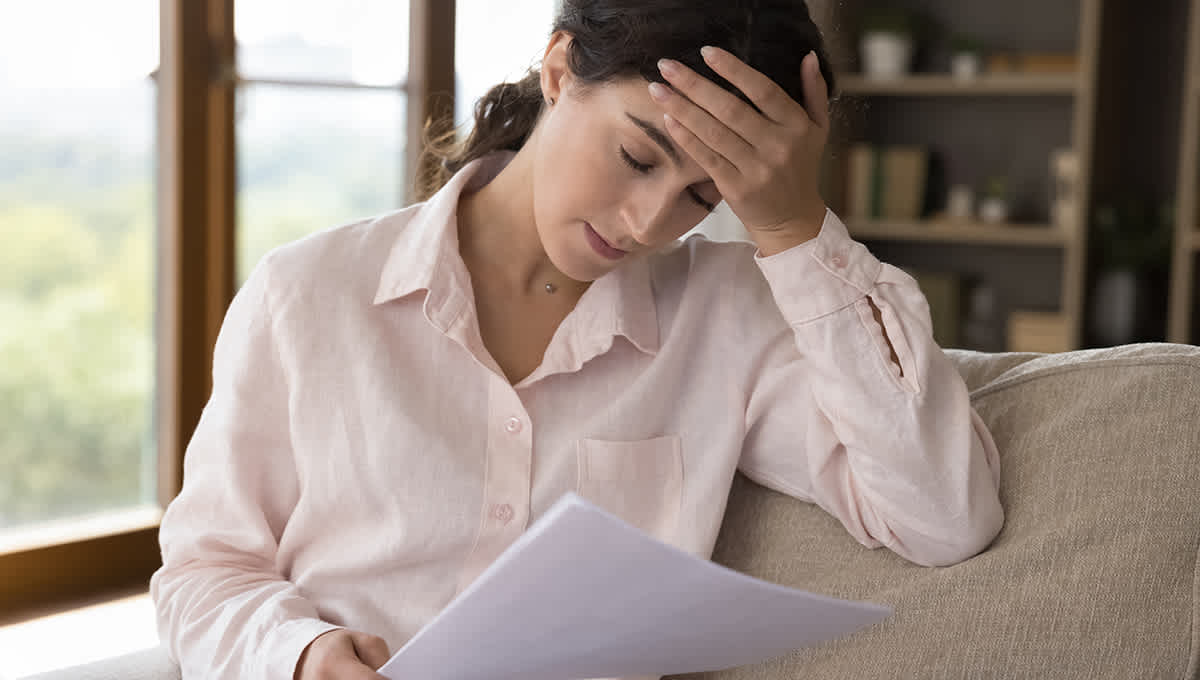 Woman sitting on couch looking visibly disappointed with hand on forehead while reviewing her home's property values.