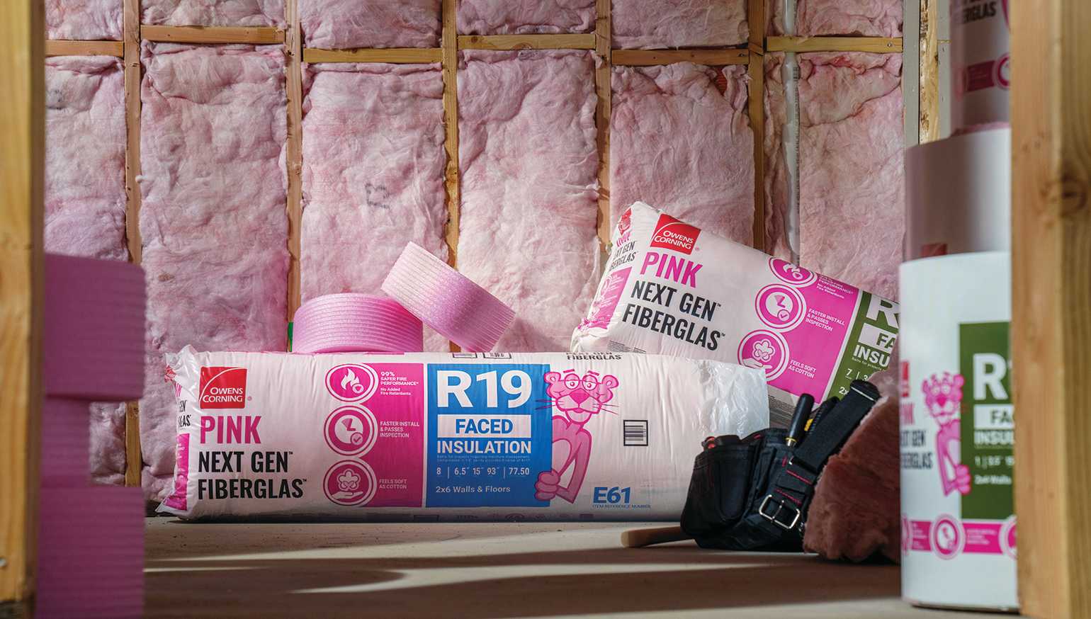 Pink insulation inside attic walls, with rolls of Owens Corning PINK Next Gen Fiberglas  on the floor
