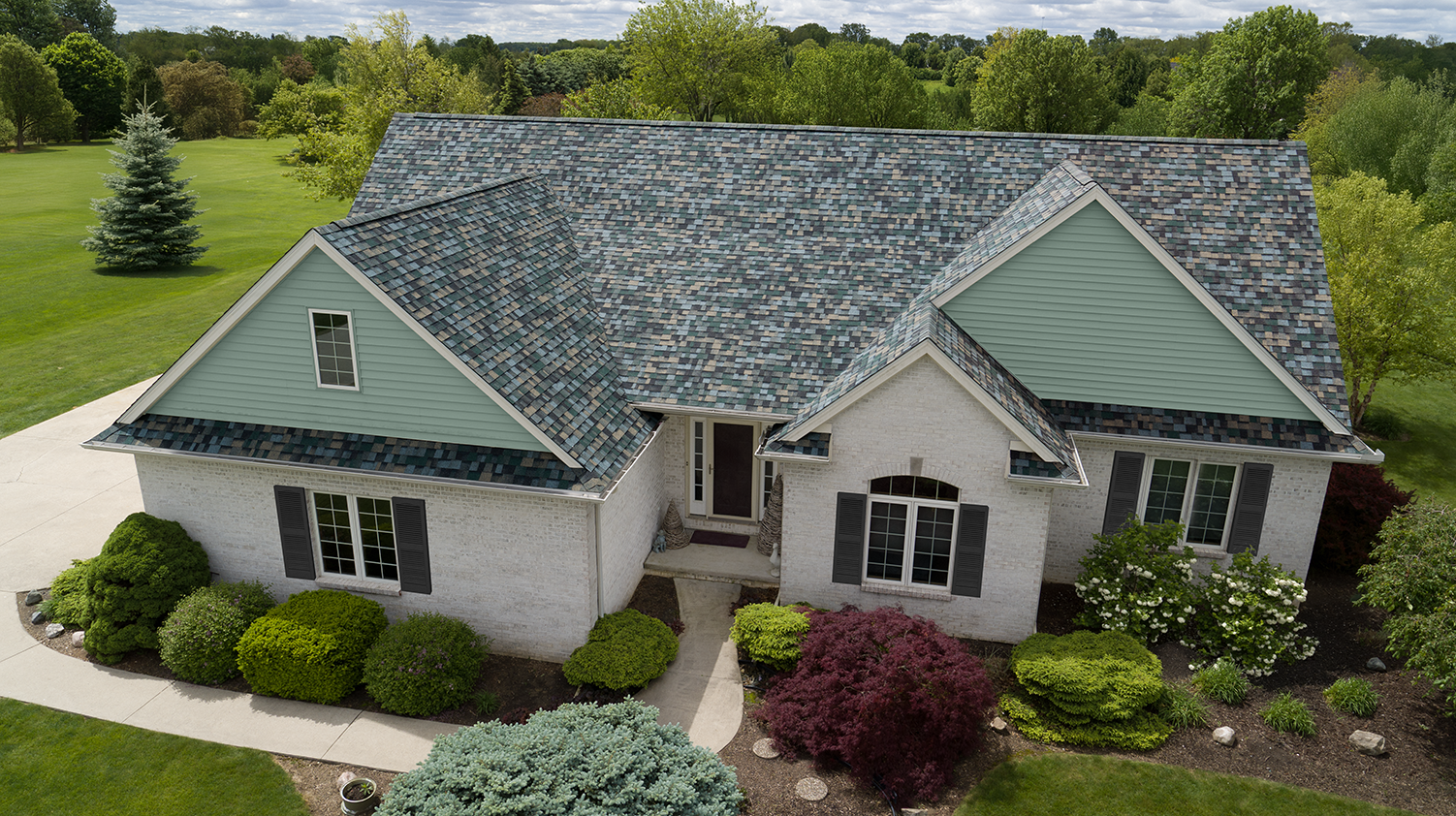 White brick home with mint green siding accents, landscaping, and Owens Corning® TruDefinition Duration® Designer shingles in Evergreen Mist