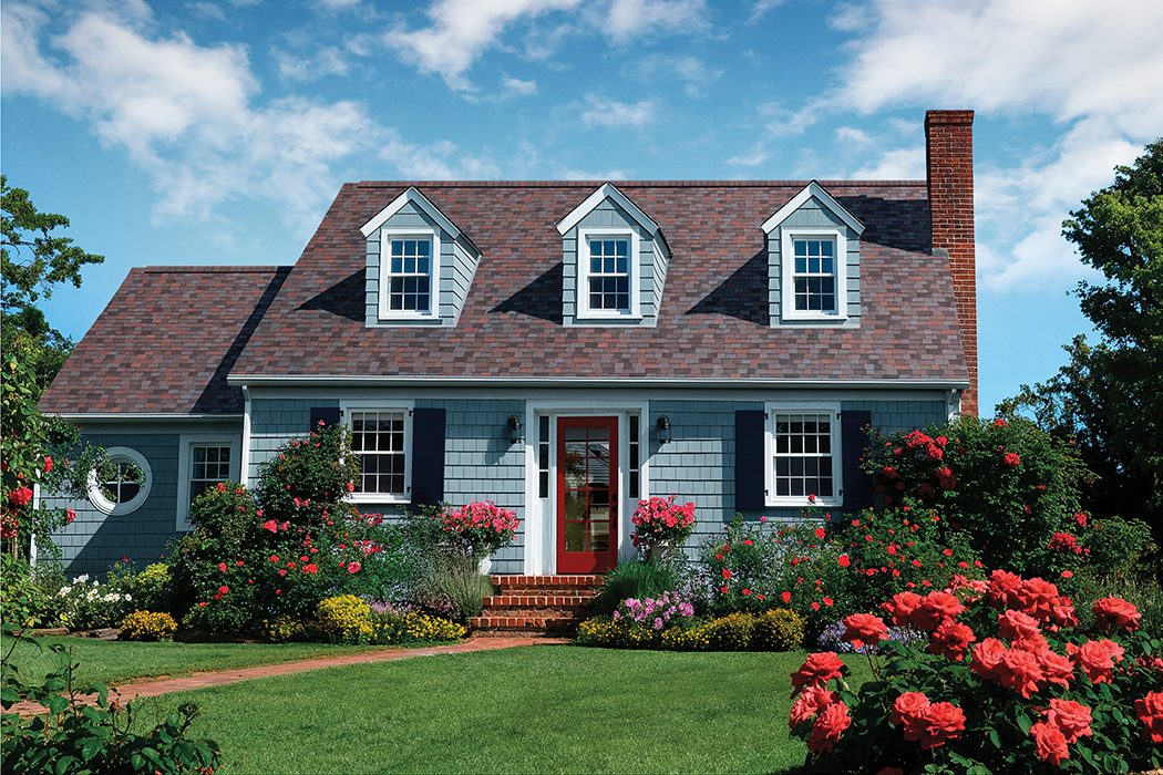 Home with blue siding, dormer windows with white trim, and Owens Corning® TruDefinition Duration® Designer shingles in Merlot