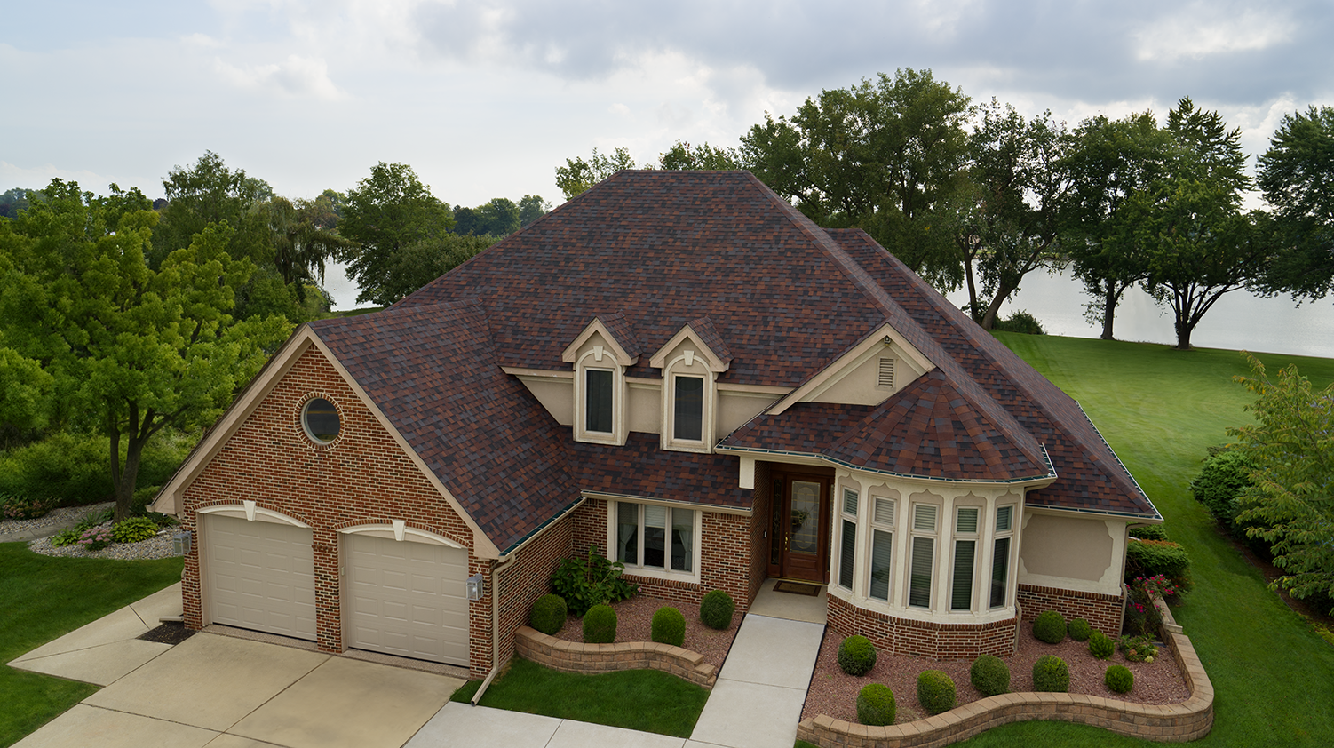 Tan house with brick and Owens Corning® TruDefinition Duration® Designer shingles in Bourbon in front of a river