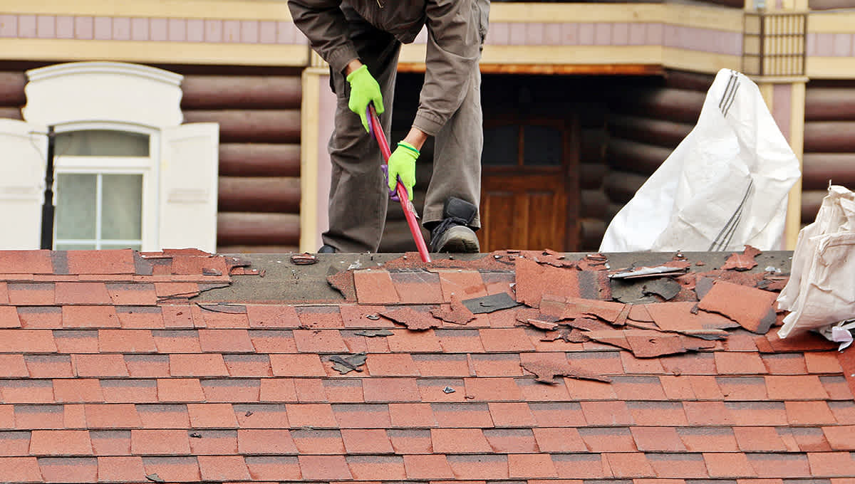 Red asphalt shingles being removed from a rooftop for recycling.