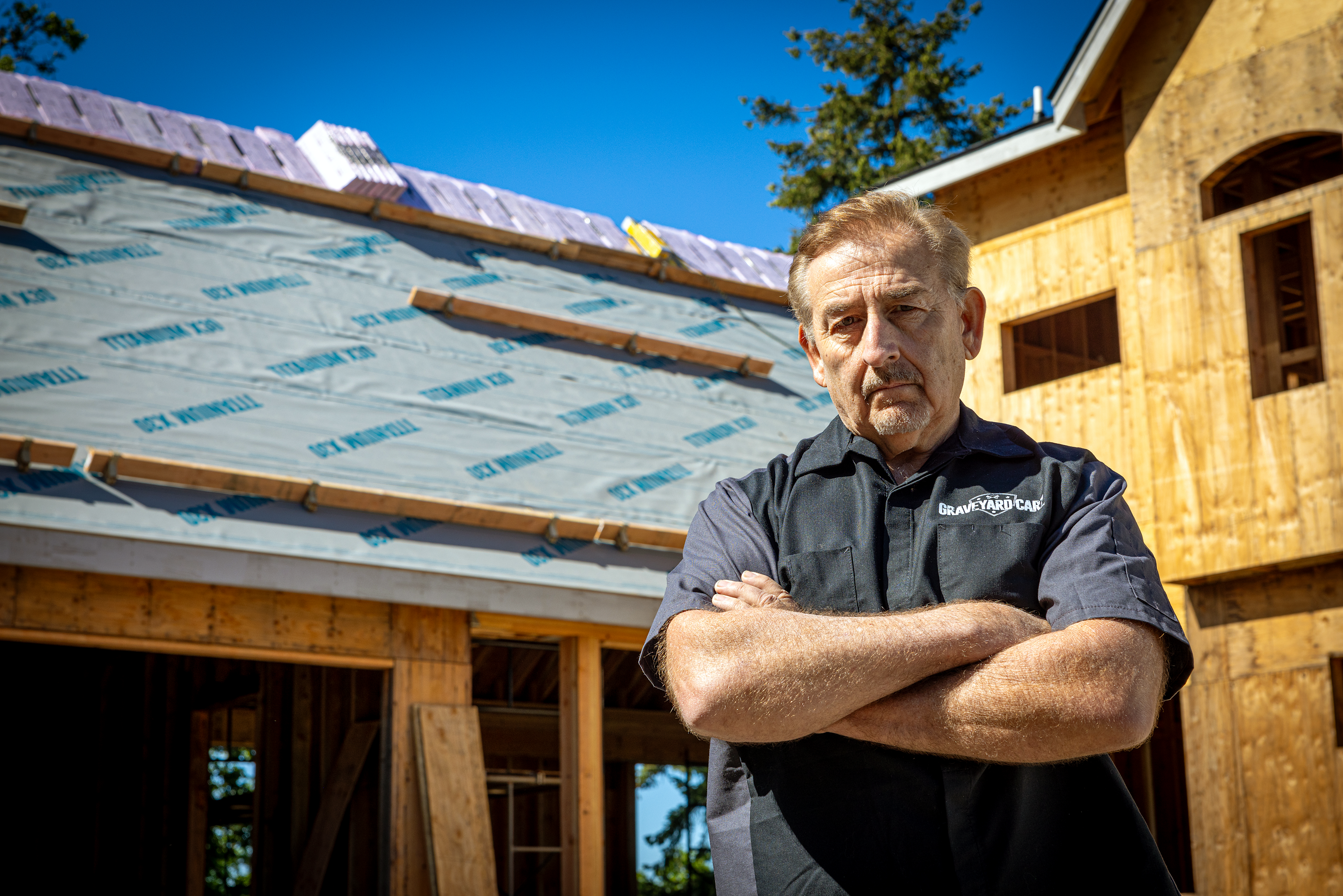 Mark Worman standing in front of his under-construction home with his arms crossed.