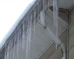 Underside angle of gutter and roofing eave covered in show with long icicles present.