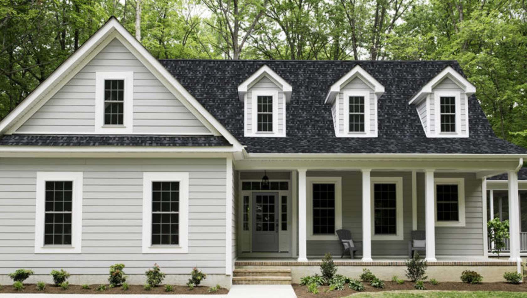 Exterior of a new Cape Cod styled suburban house with recently planted shrubs and grass