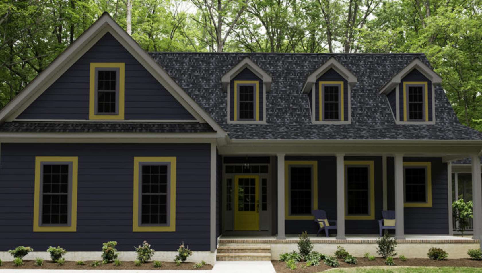 Exterior of a new Cape Cod styled suburban house with blue siding and yellow trim, recently planted shrubs and grass