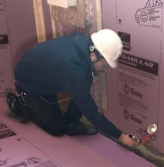 Worker applying sealant while installing pink foam insulation panels.
