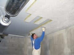 En person monterer lamellene på undersiden av betonggulvet.