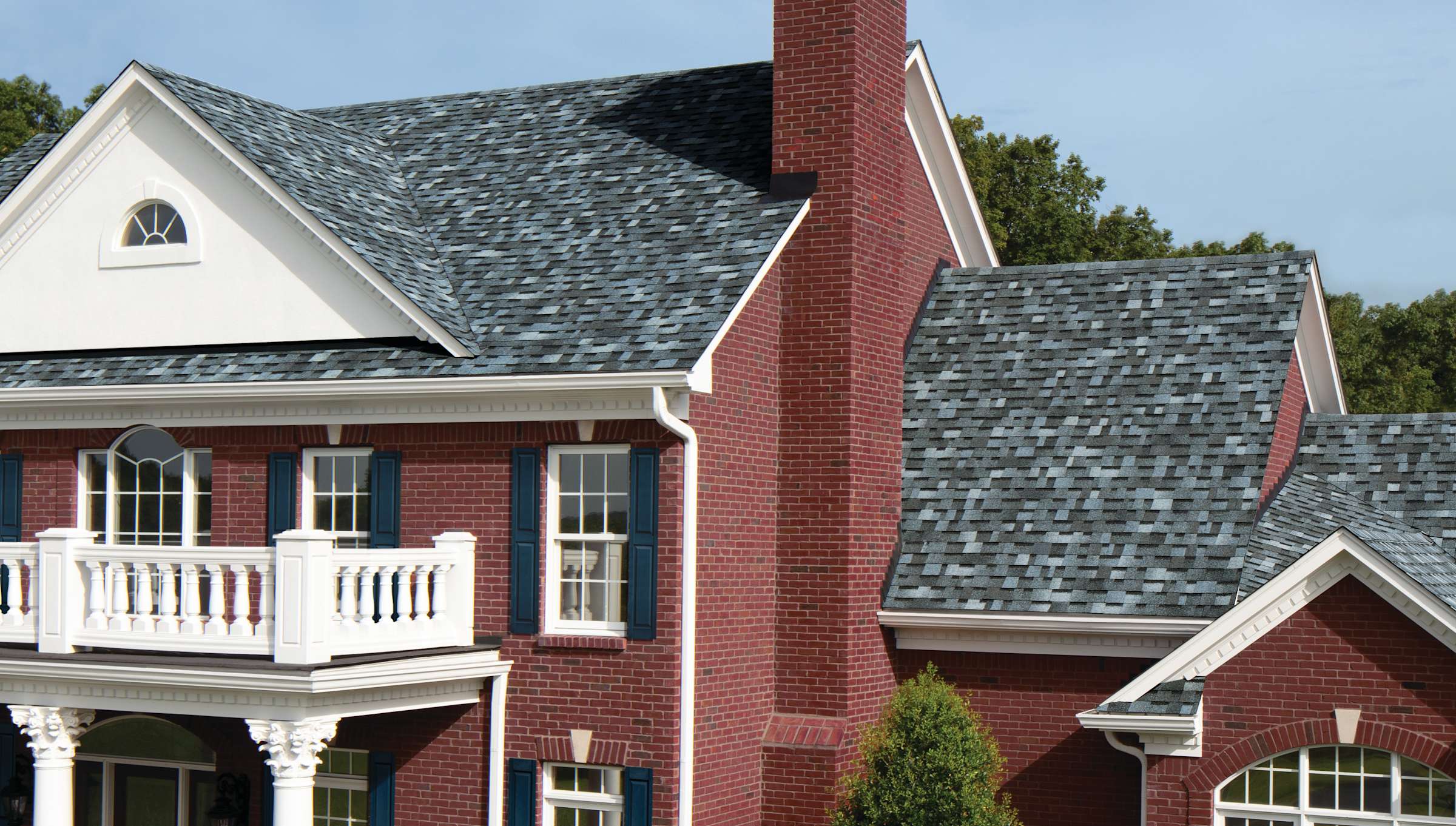 Red Brick home with white accents and second story balcony with Pacific Wave blue-toned shingles