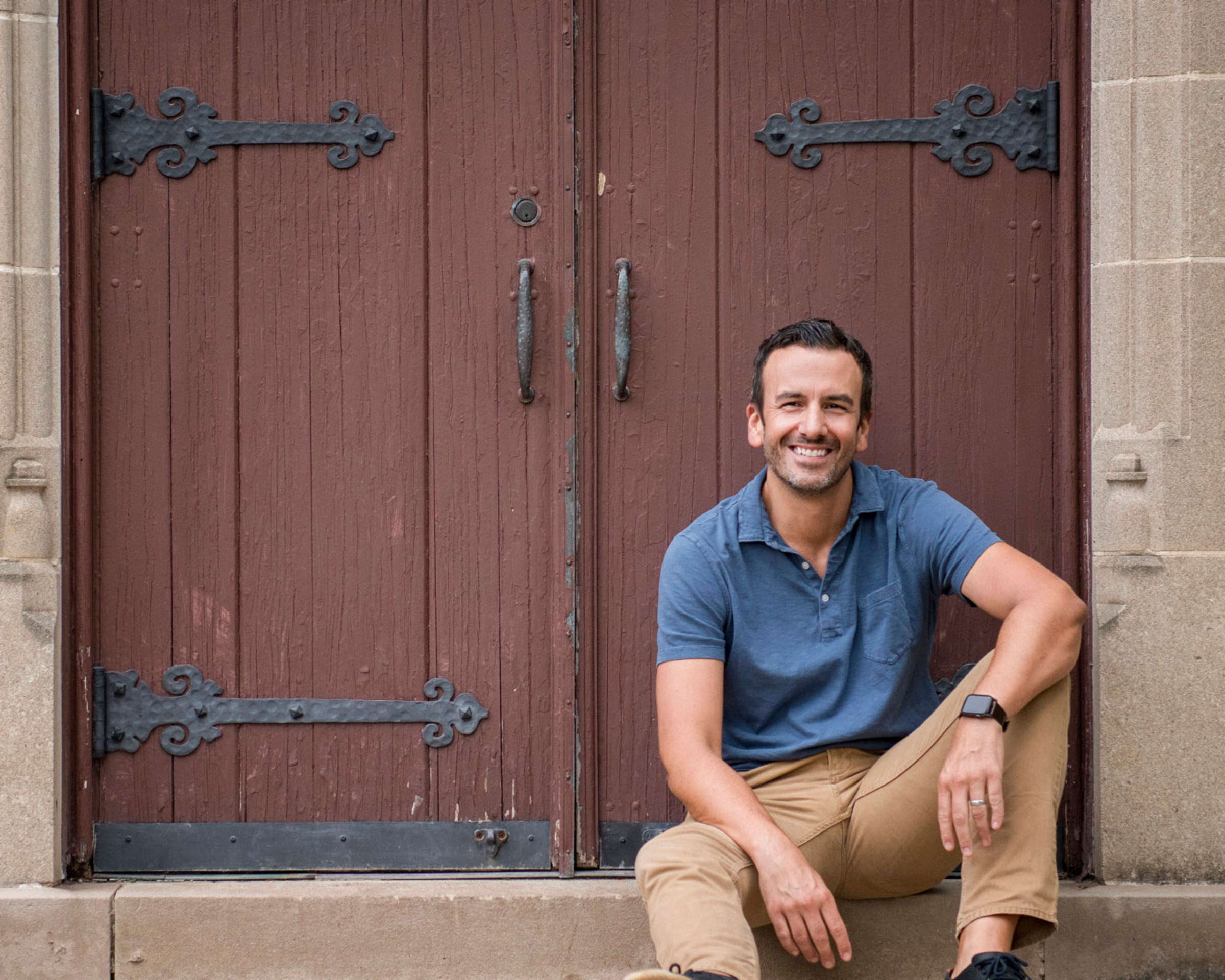 Photo of designer Chad Esslinger sitting on a step in front of a weathered red door
