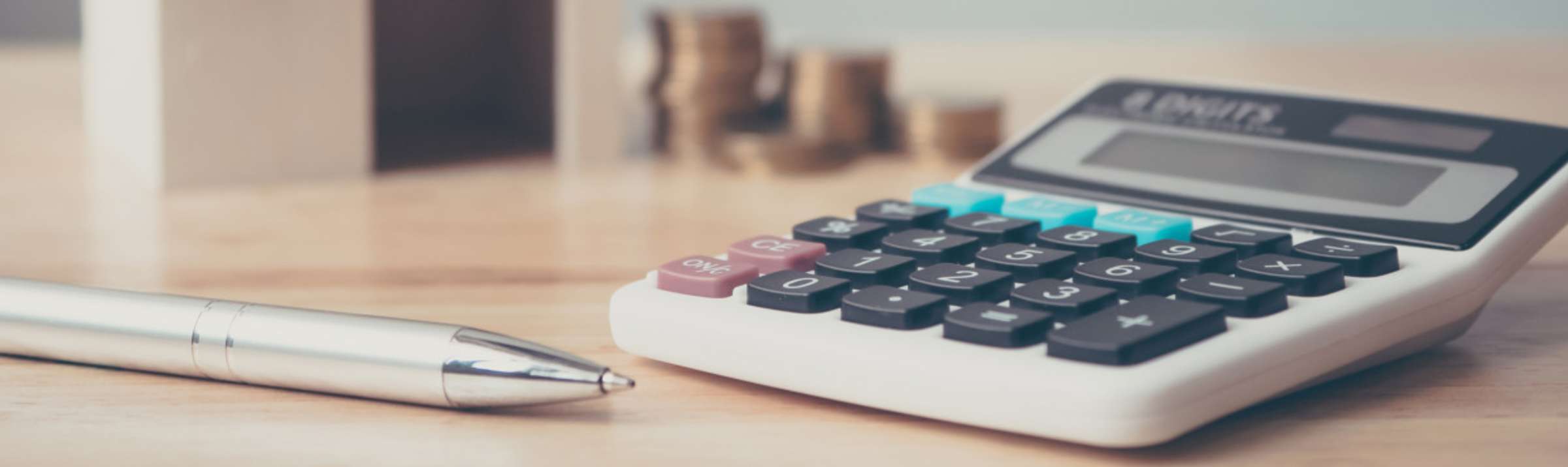 Closeup photo of a calculator sitting on a desk alongside a pen