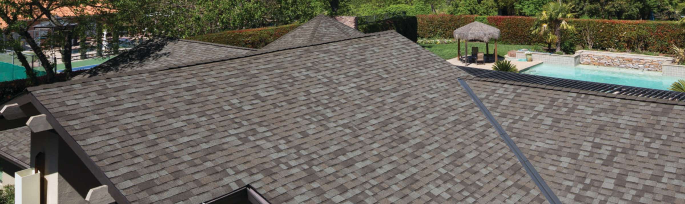 Photo of the top of a roof with COOL shingles installed, with green grass and a pool in the background