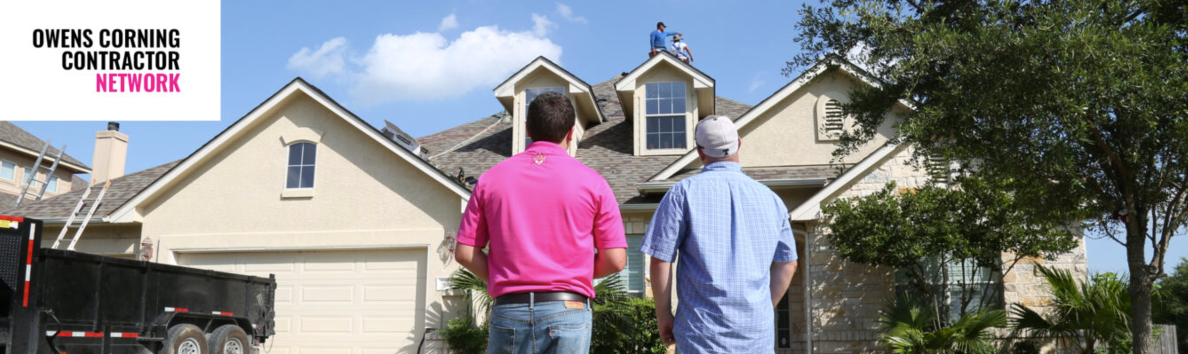 Photo of a contractor and homeowner looking at a house while roofers are working on installing shingles