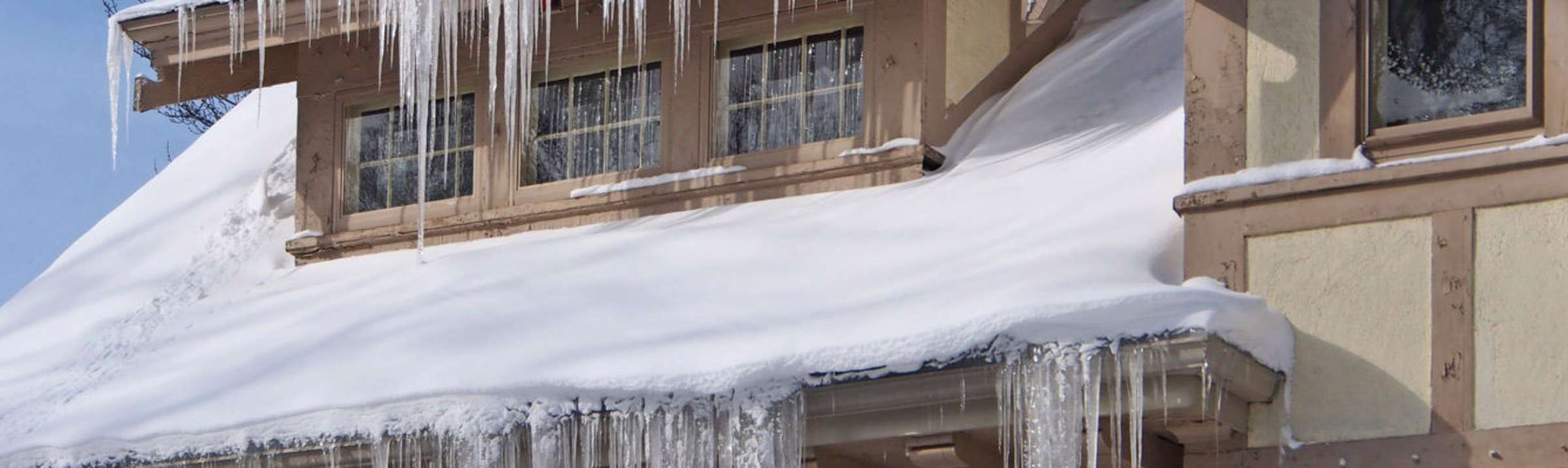 Photo of the roof of a house covered with snow, with icicles hanging