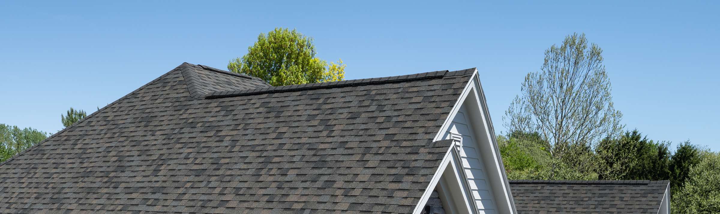 Closeup photo of a brick house with shingles that are a combination of taupe, rich brown and green-gray tones