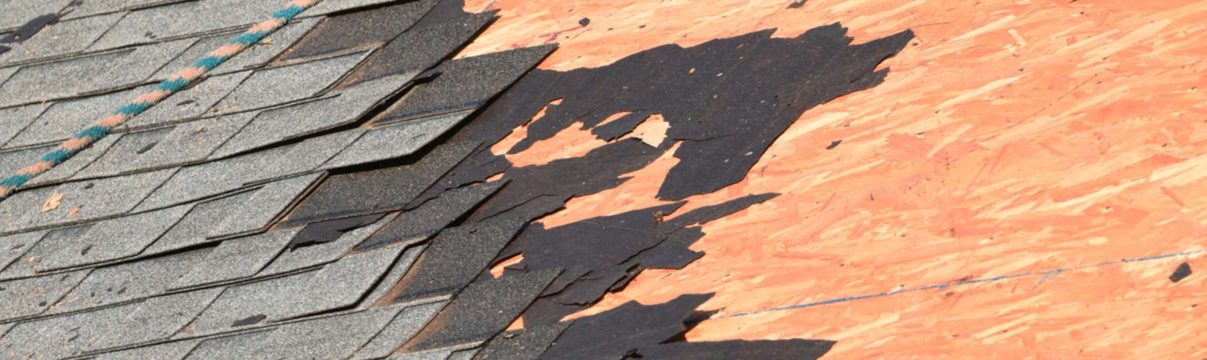Shingles being torn off a roof showing the wood decking underneath.