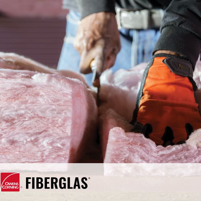 close up of a worker cutting pink fiberglass insulation