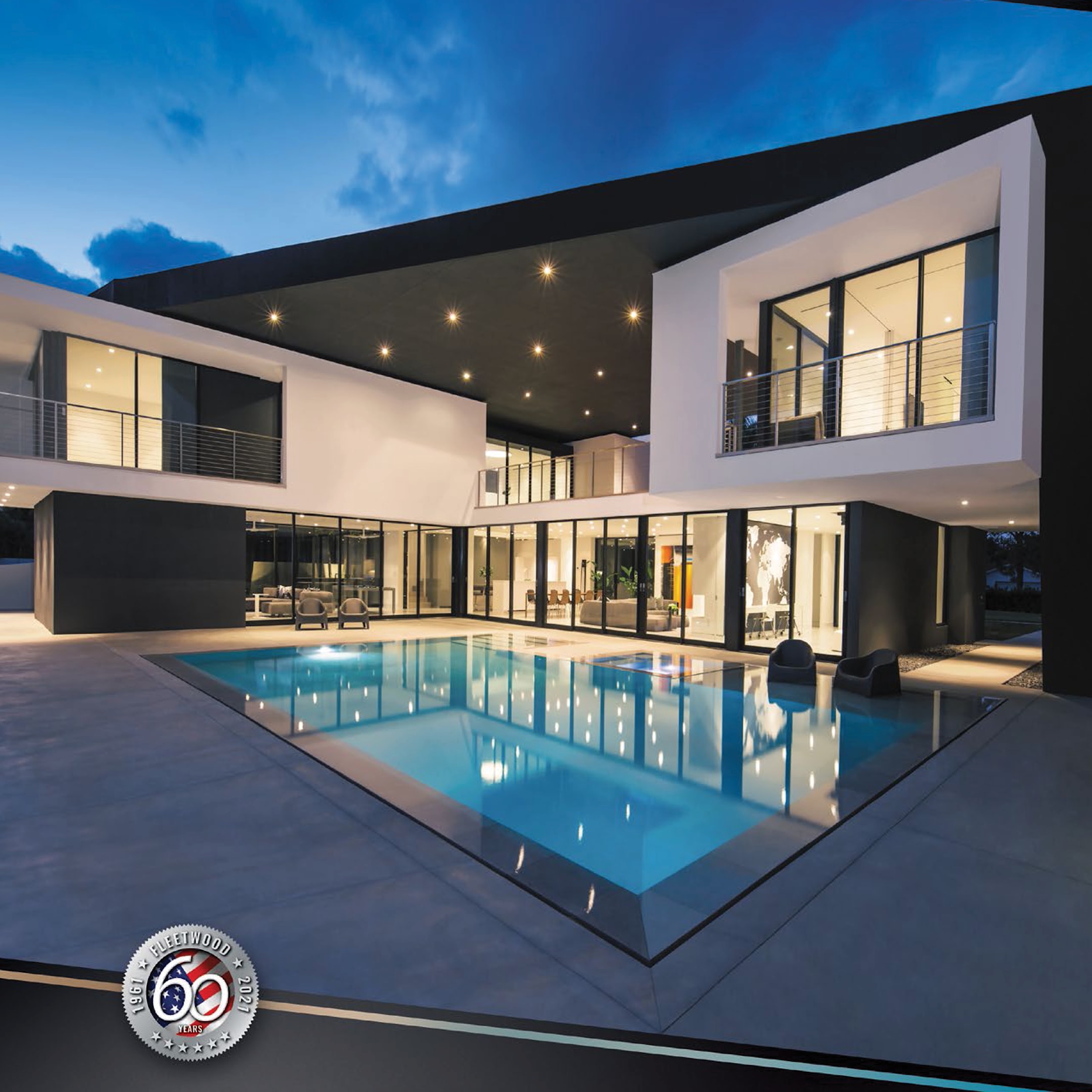 Luxury modern home with bold geometric architecture, white stucco exterior, black trim accents, and expansive floor-to-ceiling glass windows surrounding a large illuminated swimming pool at dusk.