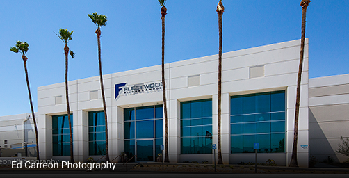 Exterior view of Fleetwood building with modern architecture, large glass windows, and tall palm trees under clear blue sky.