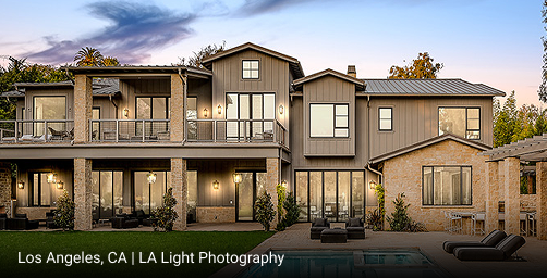 Luxury modern farmhouse in Los Angeles, California featuring multi-gabled roof design, gray board-and-batten siding, natural stone accents, and expansive glass doors opening to outdoor living space with pool and pergola.