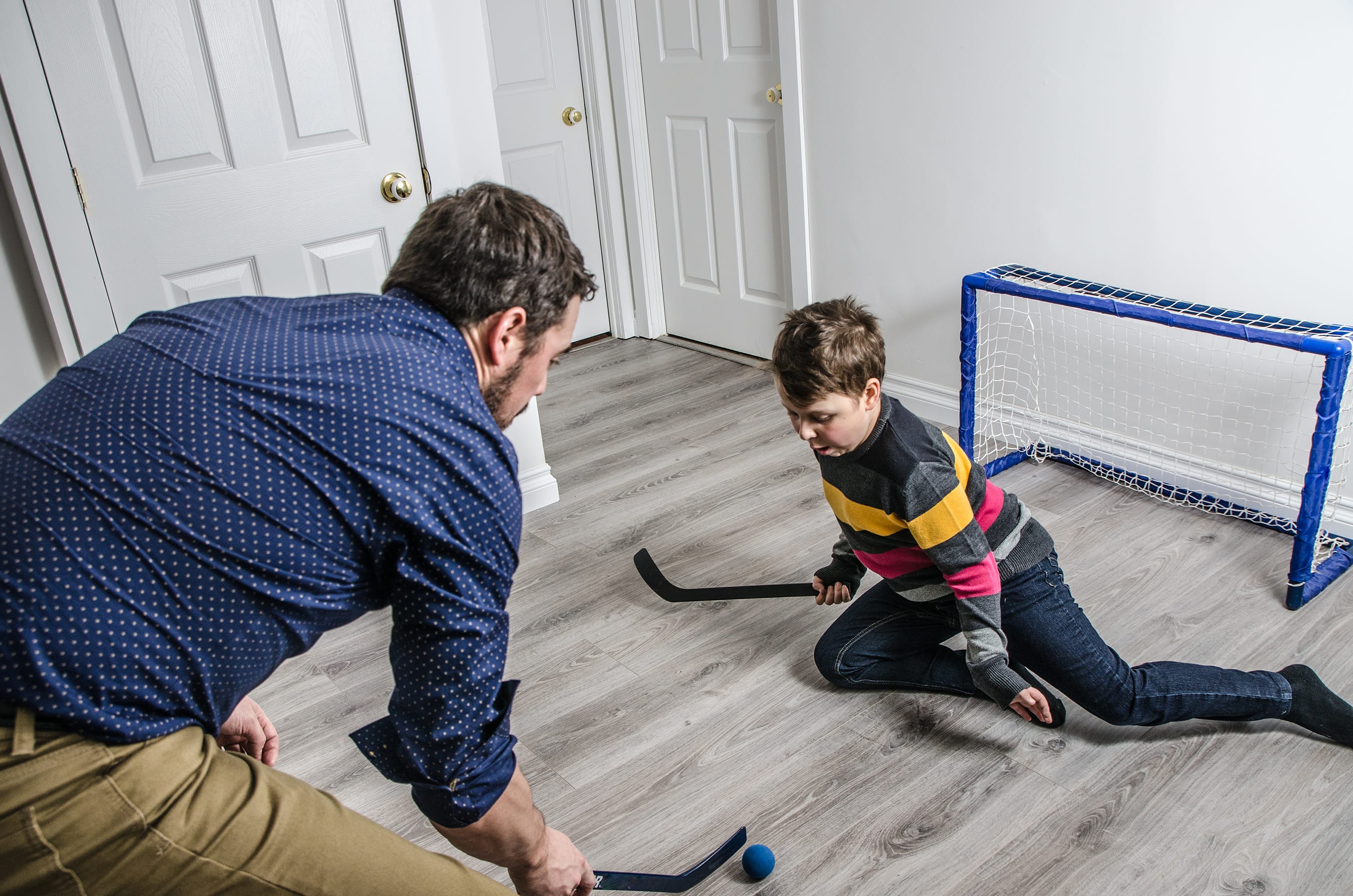 A father and son playing with a toy hockey set in their home