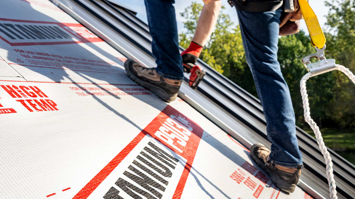 A roof that is partially finished showing the Titanium underlayment exposed and contractor walking across the roof slope.