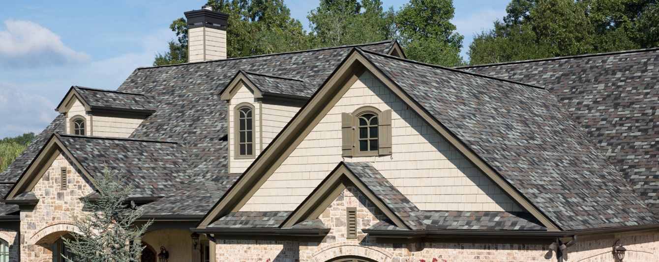 Home with tan wood shake siding, brown trim and Owens Corning Duration Designer roof in Storm Cloud