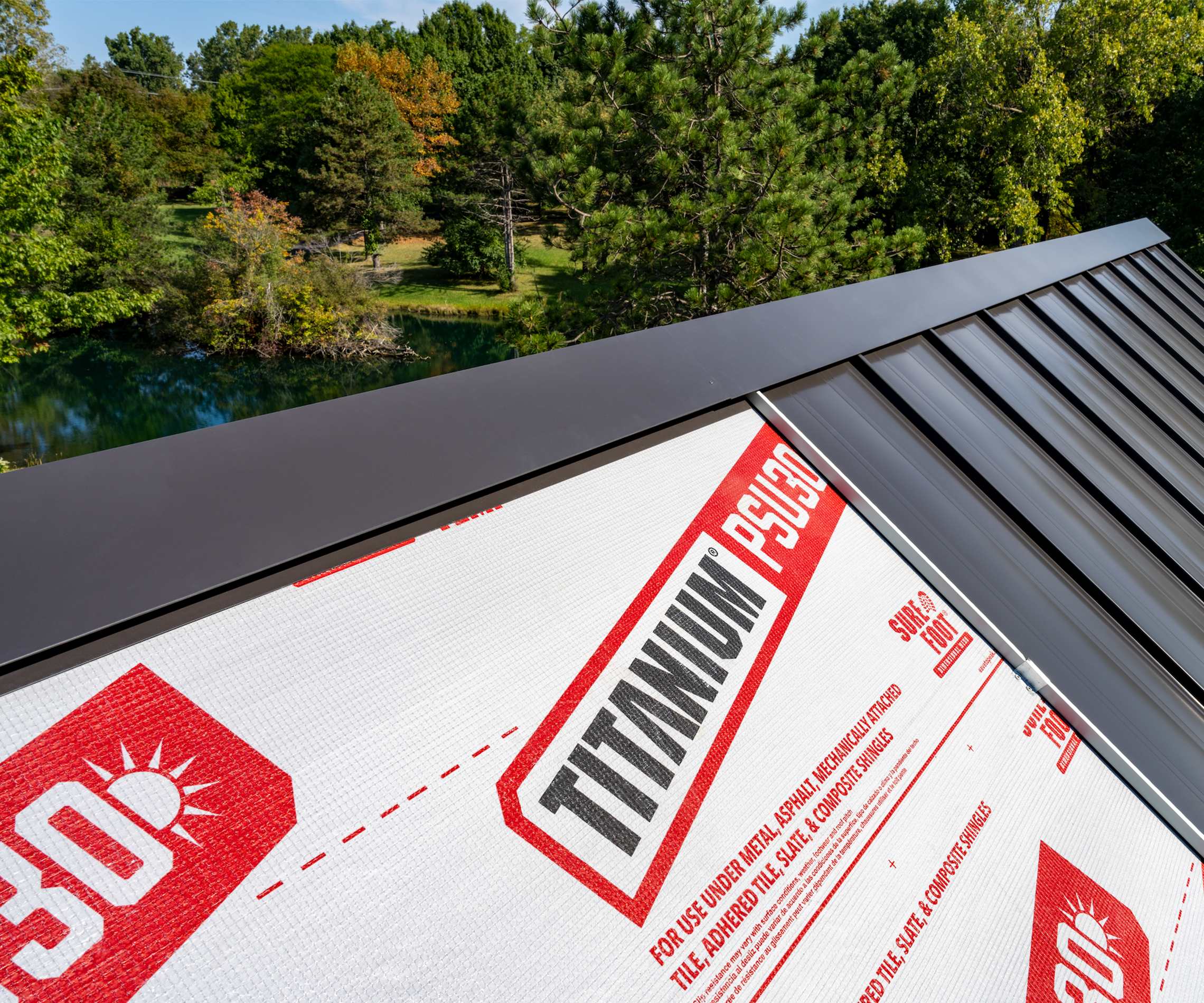 Close-up of a dark metal roof installation over TITANIUM® PSU30 roofing underlayment, with trees in the background.