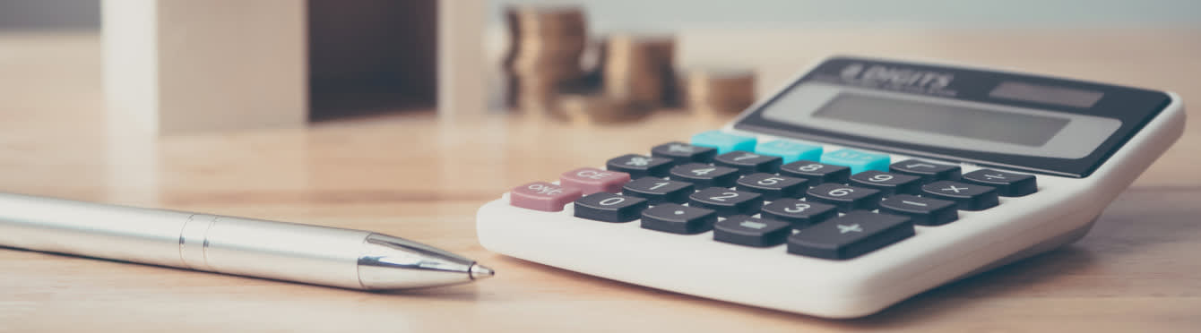 Closeup photo of a calculator sitting on a desk alongside a pen