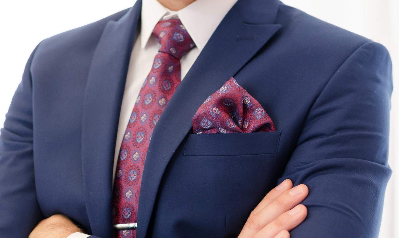 Photo zoomed in on the chest of a man wearing a navy blue suit with red patterned tie
