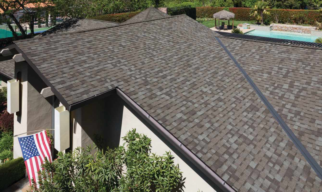 Photo of the top of a roof with COOL shingles installed, with green grass and a pool in the background