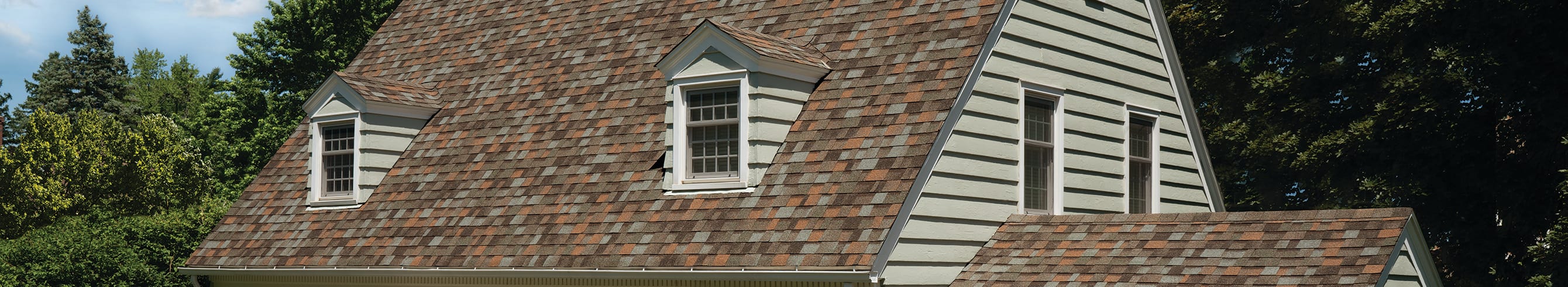 House with tan siding, two dormers with tan windows and Owens Corning Aged Copper shingles.